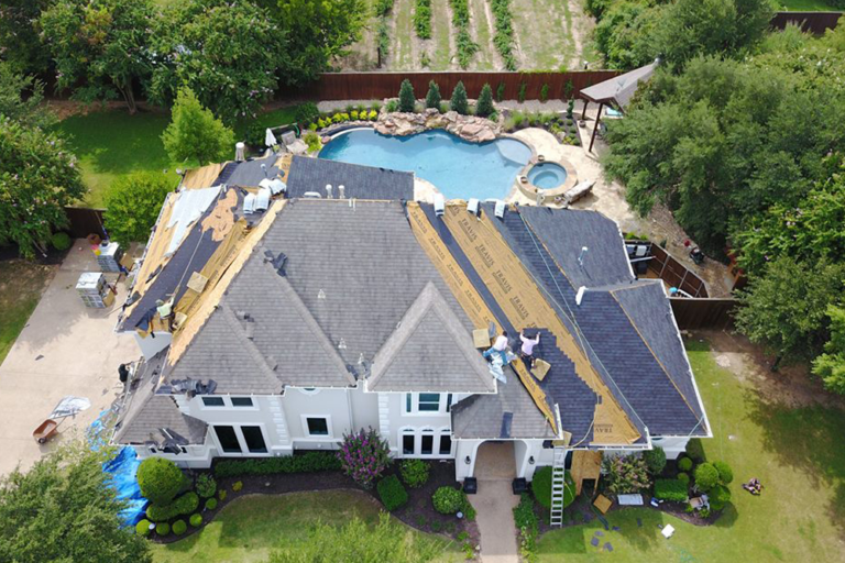 Aerial view of a large home during a roof replacement, with a pool and backyard